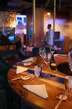 Warmly lit, elegant restaurant scene featuring wooden tables set for dinner with glassware and napkins.