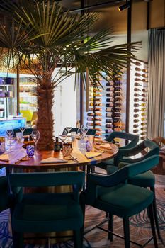 Luxury dining area with a palm tree centerpiece, surrounded by teal chairs in an upscale restaurant.