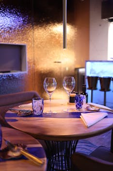 A stylish indoor dining table with glassware and utensils set for two, in a contemporary restaurant setting.