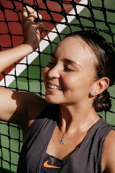 阳光下，一名年轻女子闭着眼睛，在网球场边开心地微笑着