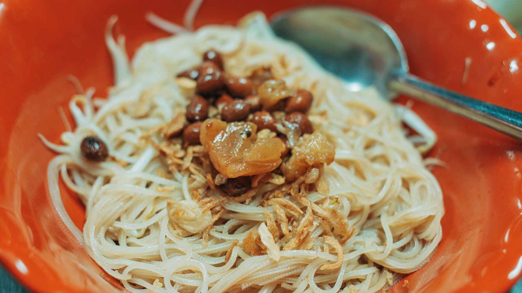 Close-up of a tasty Asian noodle dish with savory toppings served in a red bowl.