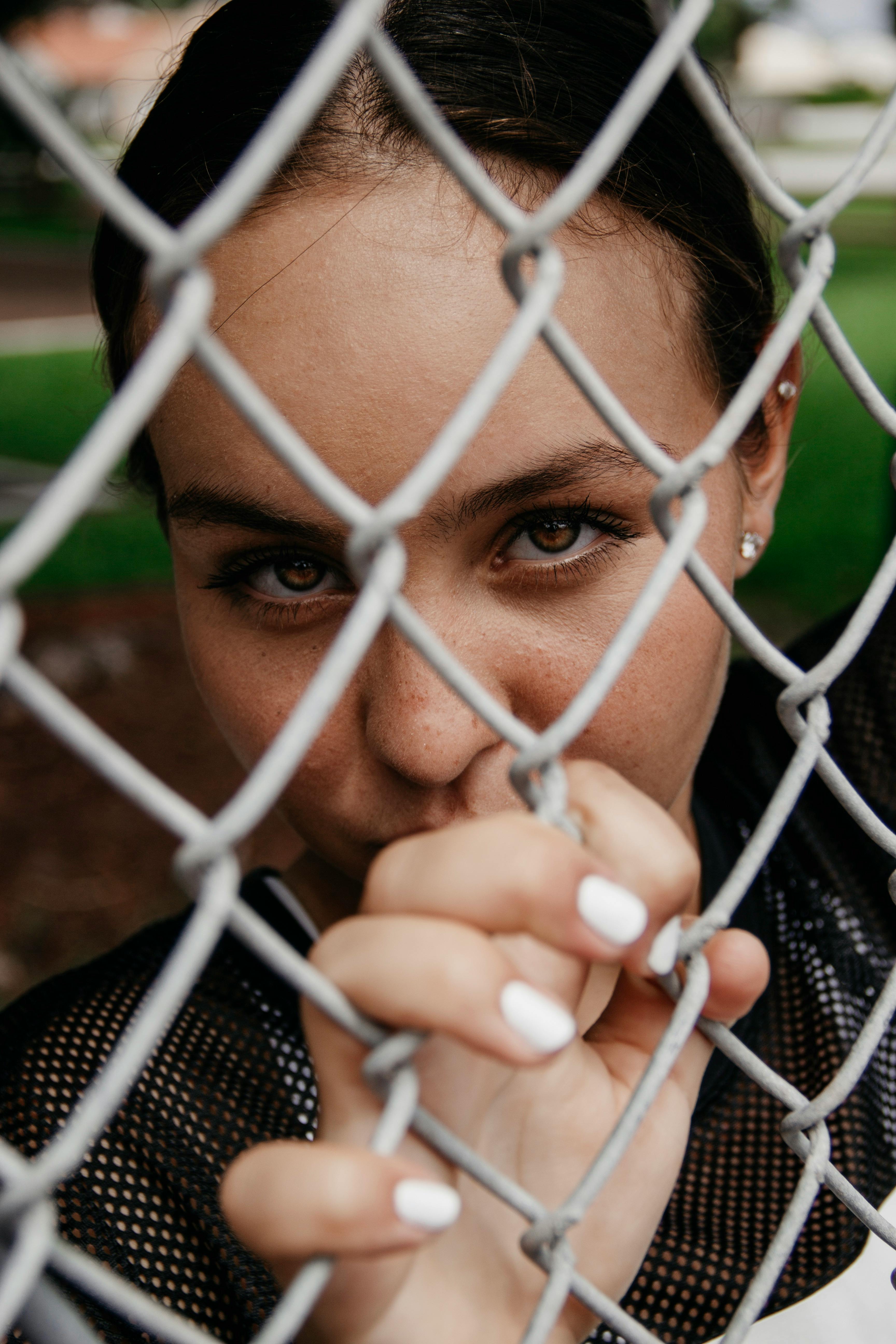 close up portrait photo of woman leaning on chain link fence