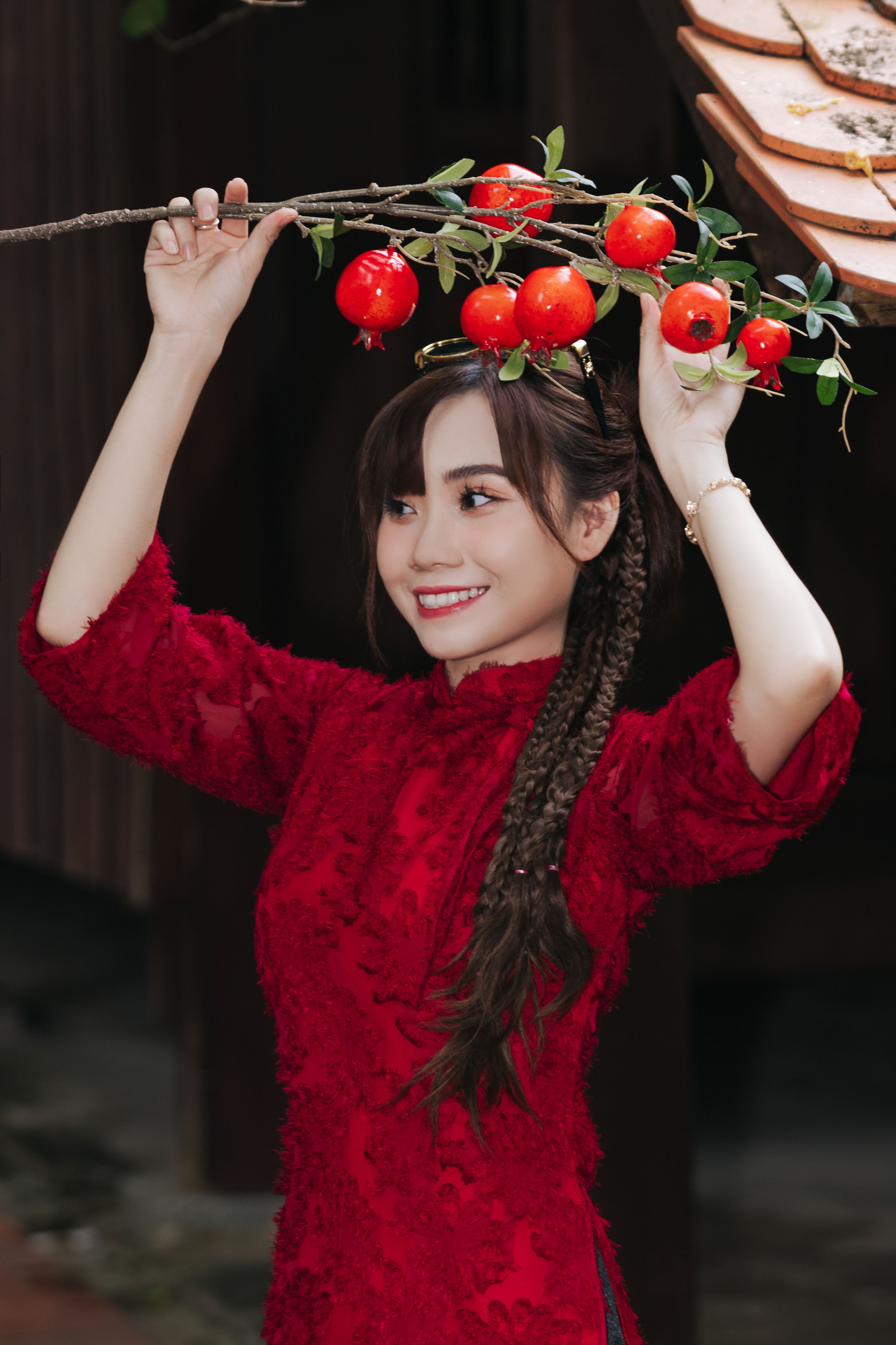 Smiling woman in red traditional dress holding a branch adorned with vibrant red fruits.