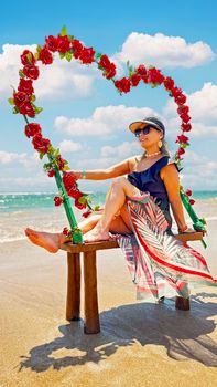 Woman enjoys sunny day on beach, sitting on rose heart chair.