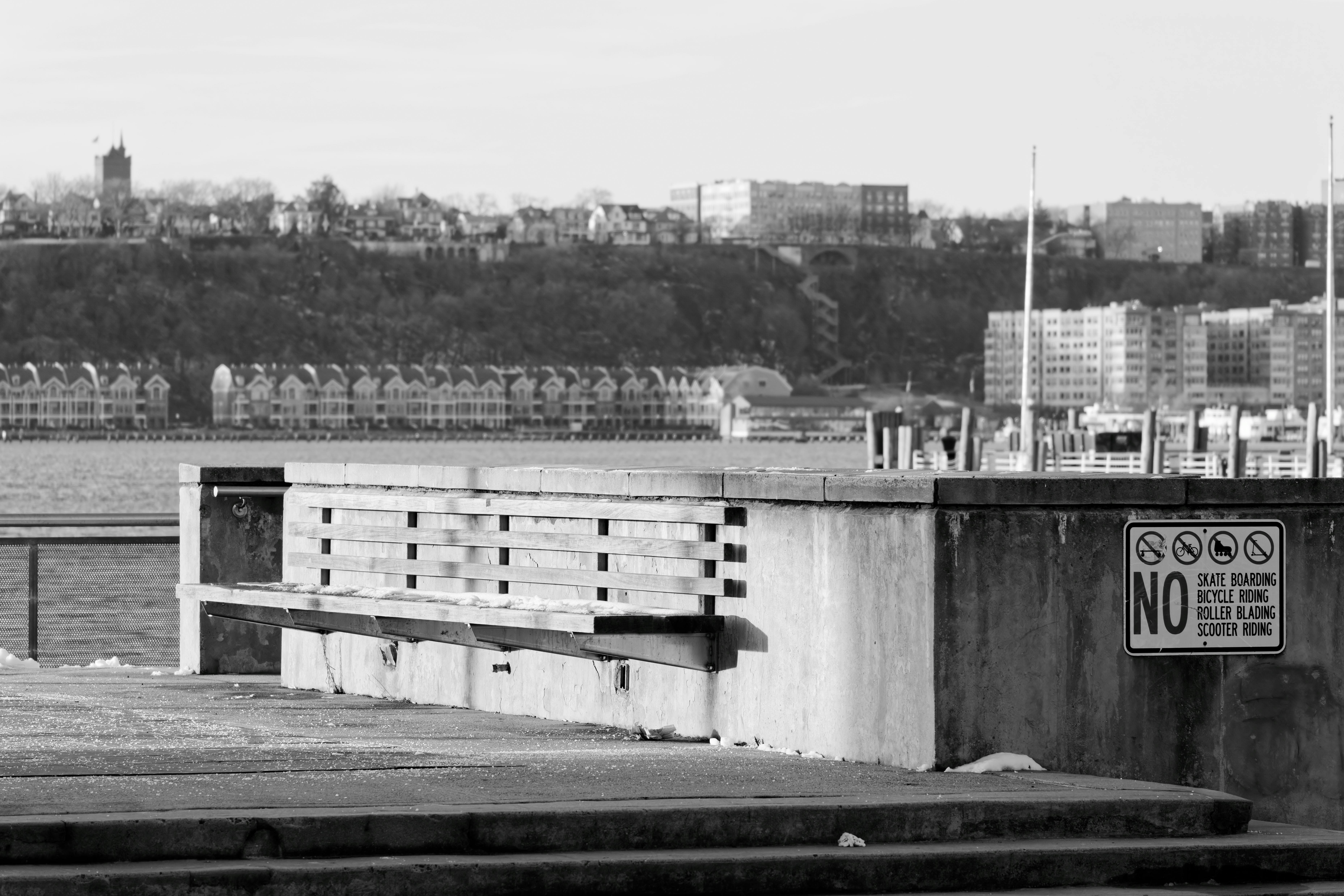 Minimalist cityscape with empty bench and no skateboarding sign by the river.