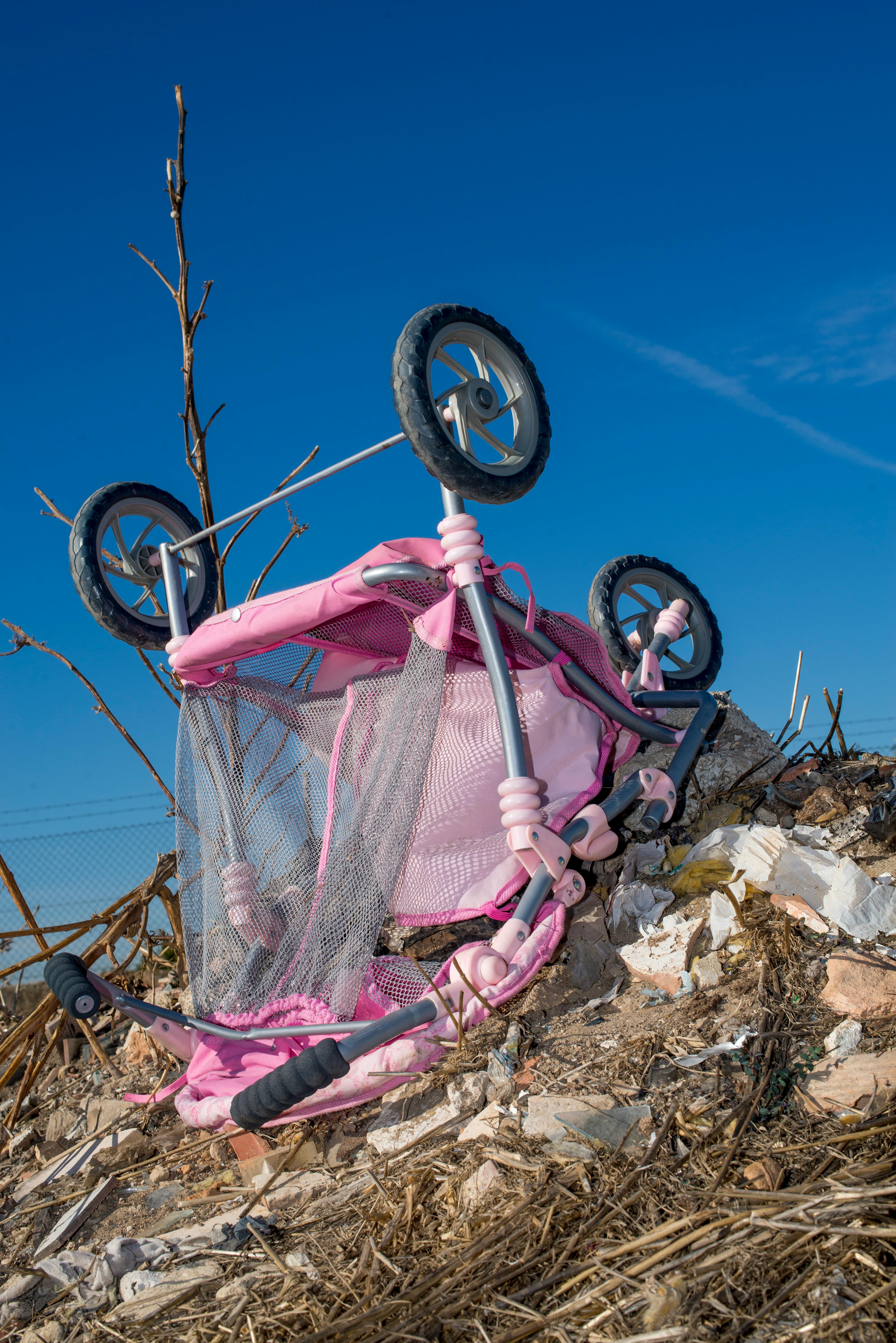 abandoned pink stroller on debris outdoors