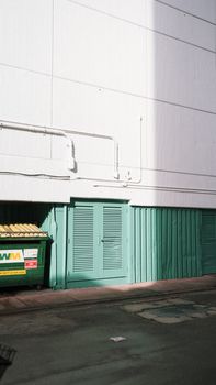 Empty urban alleyway with green doors and a green dumpster against a building wall.