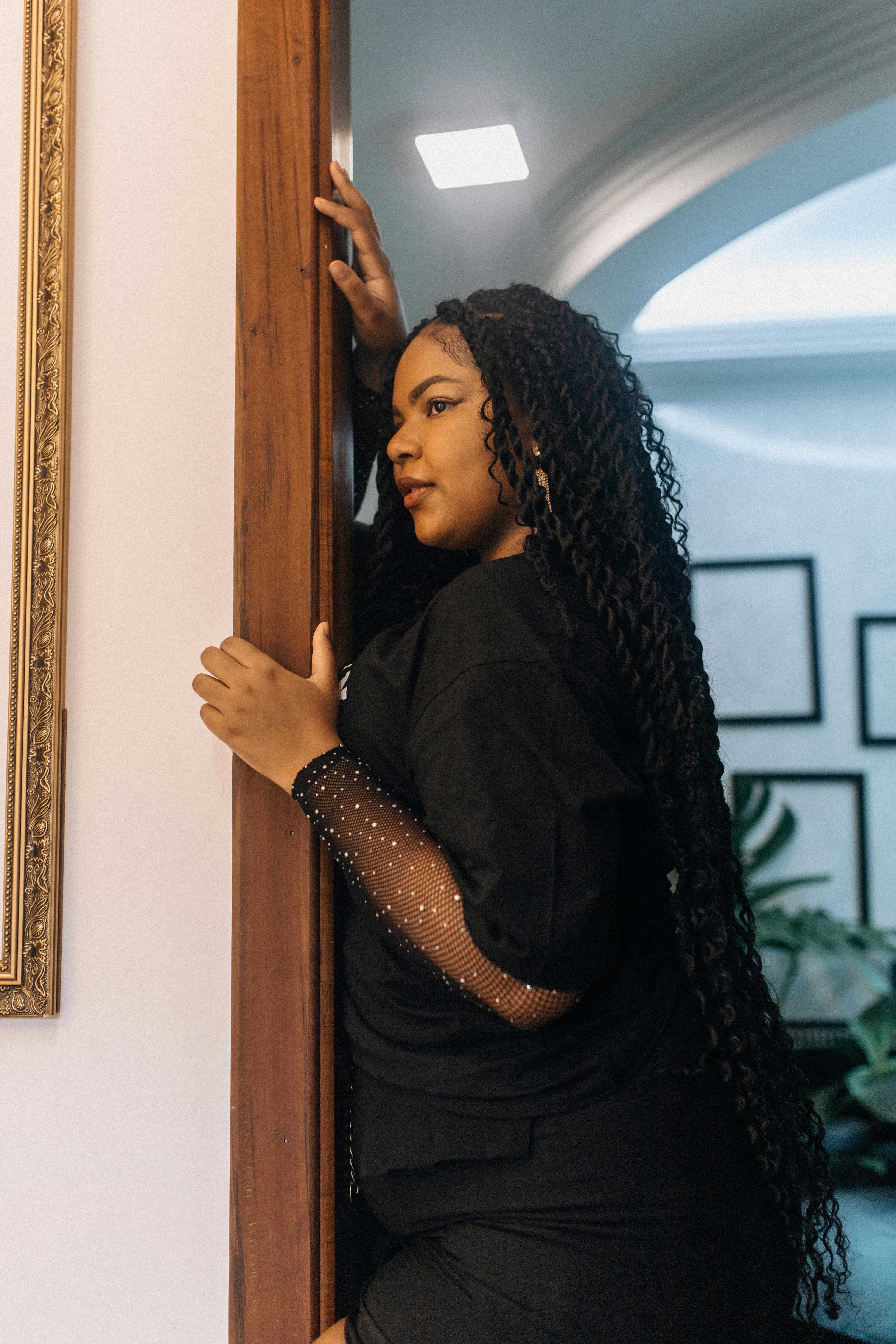Confident woman with long braids posing indoors against a stylish background.