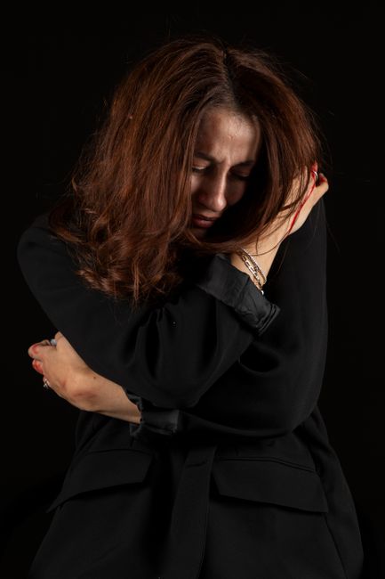 Fotomural Retrato emocional de una mujer abrazándose a sí misma en una habitación oscura, transmitiendo tristeza.