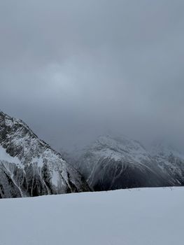 Moody winter mountains shrouded in clouds against a snowy backdrop.