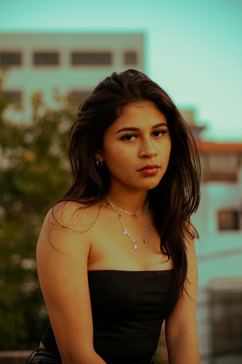 Free Portrait of a young woman in a stylish outfit in an urban outdoor setting with modern buildings. Stock Photo