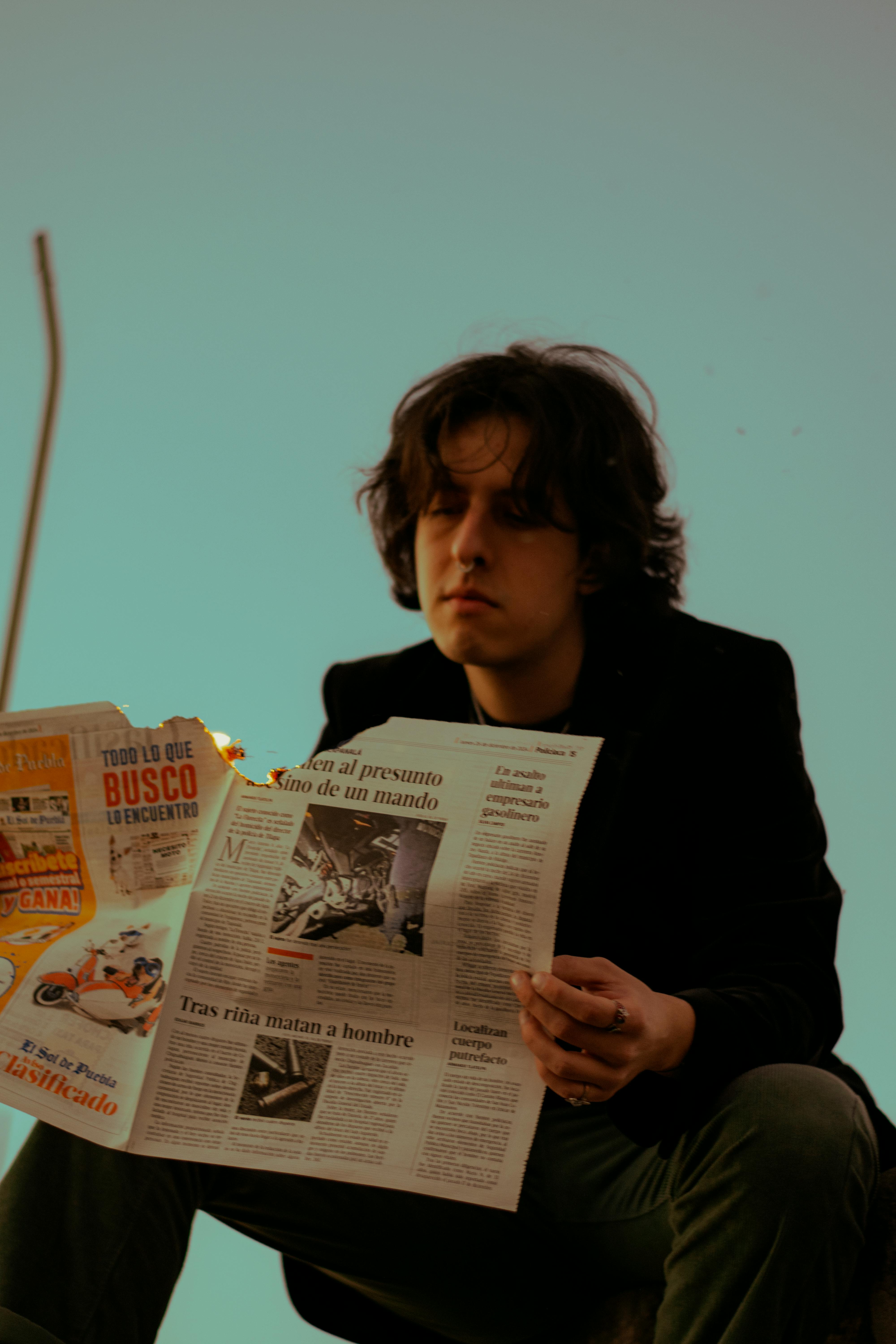 young man reading newspaper outdoors at dusk