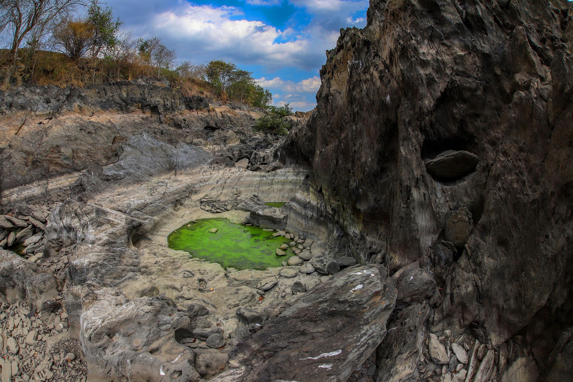 Explore a striking rocky terrain featuring a vibrant green algae pool under a clear sky.