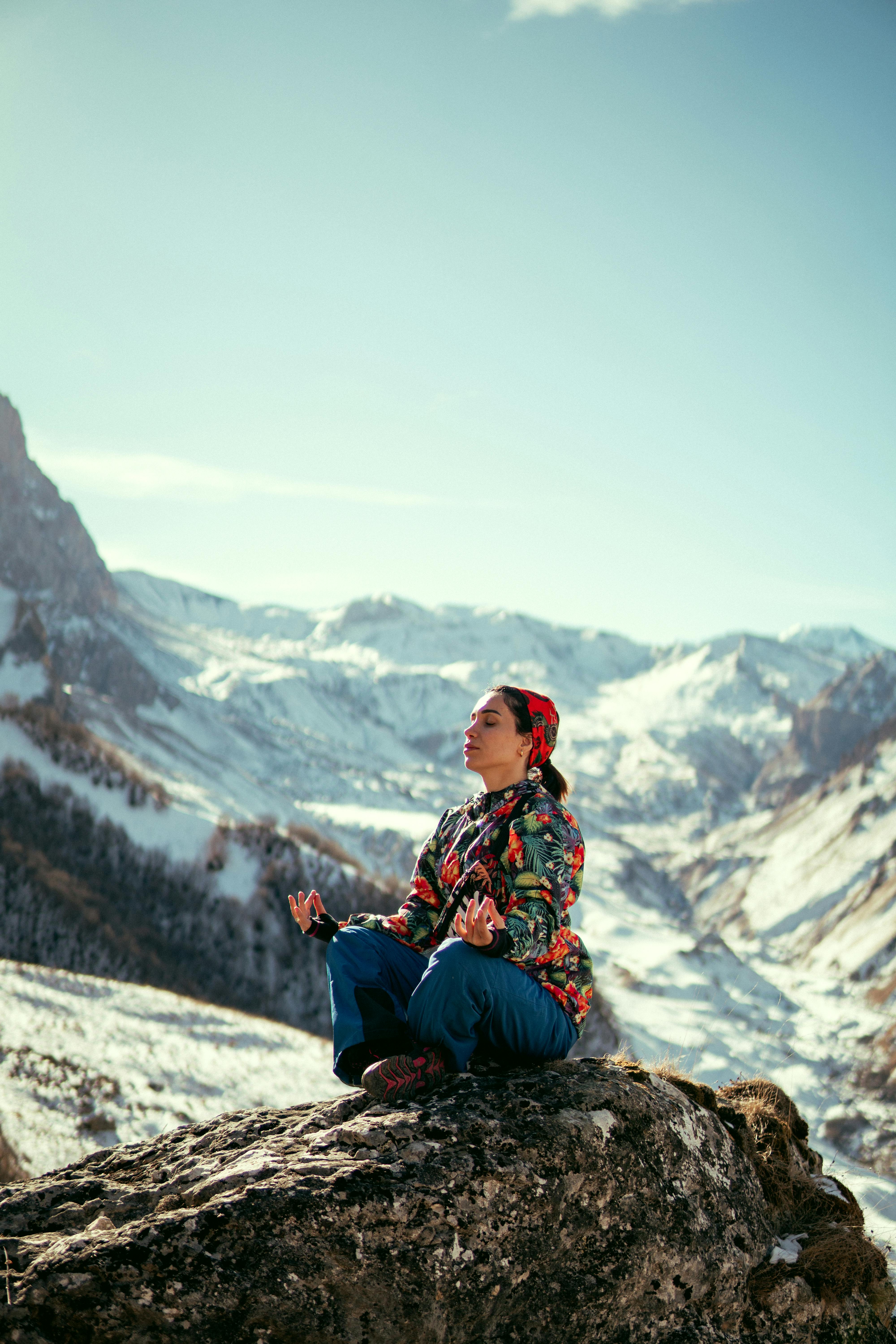 A woman meditates peacefully on a rock in the snow-capped Qusar mountains, Azerbaijan.