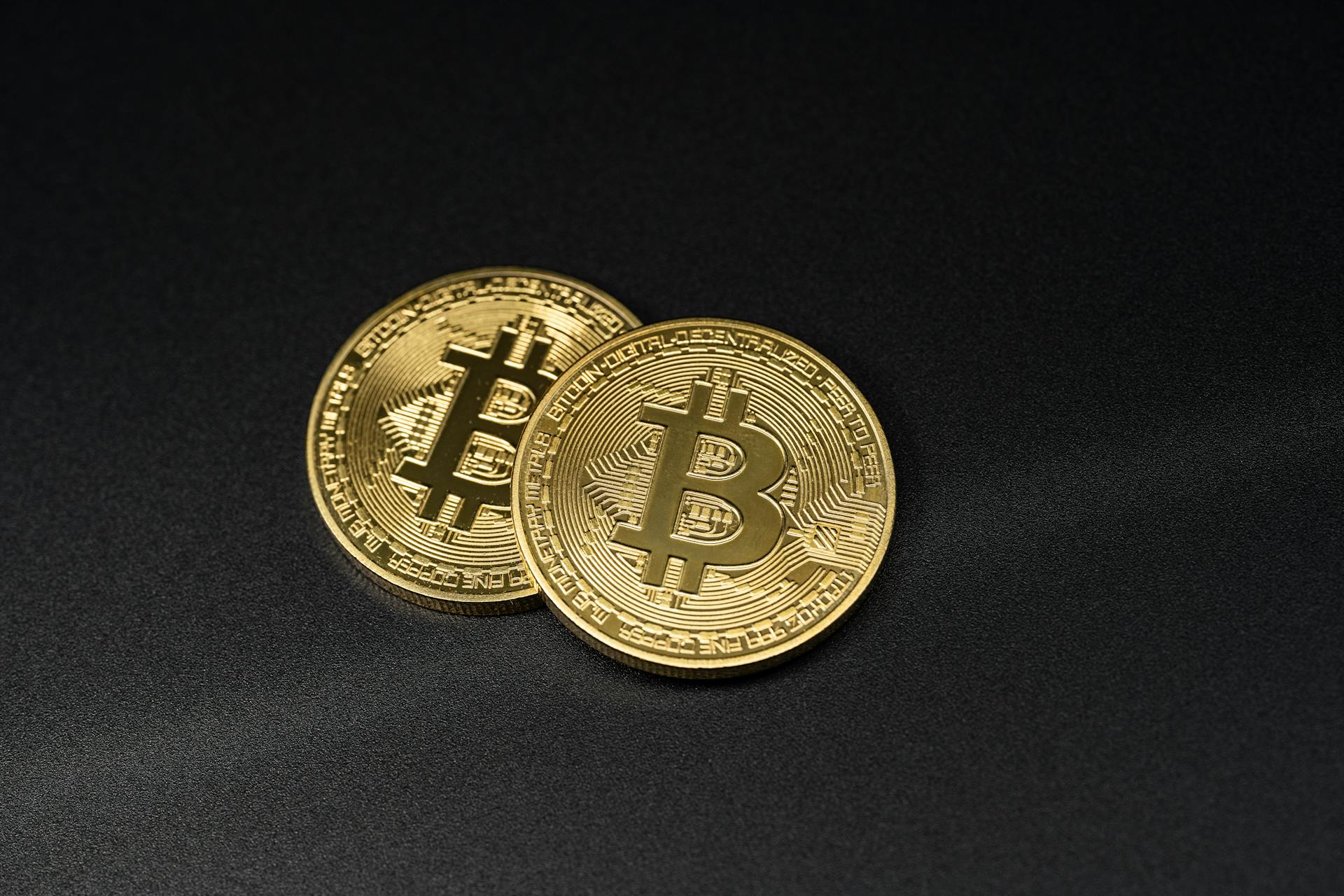 Two gold Bitcoin coins resting on a sleek black surface, symbolizing digital currency.