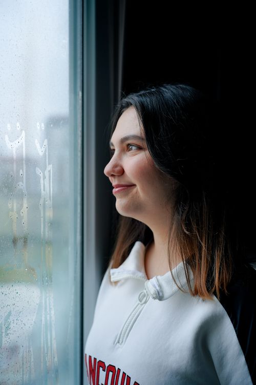Free A young woman looking thoughtfully out a rainy window with smiley faces drawn on it. Stock Photo