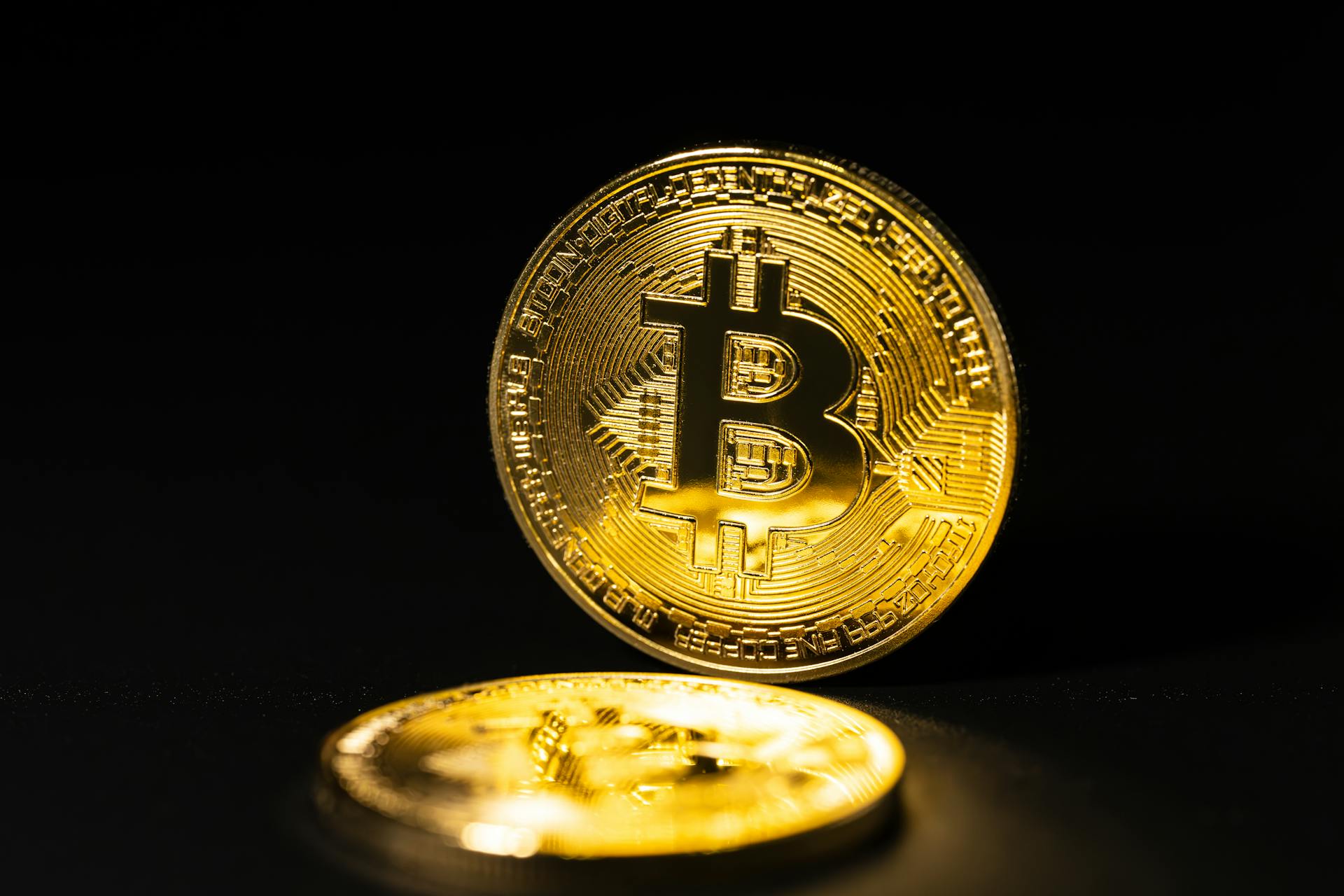 Close-up of two golden Bitcoin coins on a dark reflective surface, highlighting cryptocurrency symbolism.