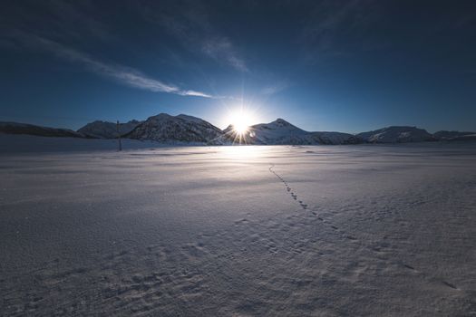 Snow-capped mountains with footprints at sunrise, capturing a serene winter landscape.
