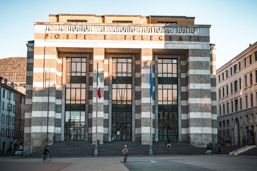 Front view of the historic Italian post office building in Brescia, Italy, with flags and pedestrians.