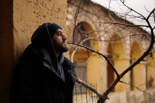 Free A man in winter attire leans against a rustic wall, gazing into the distance. Stock Photo