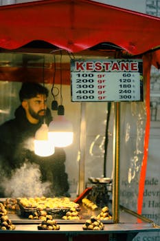 A street vendor selling roasted chestnuts under warm lights on a cool evening.
