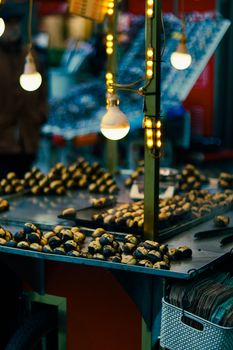 Street market stall illuminated with lights, displaying freshly roasted chestnuts. Warm ambiance.