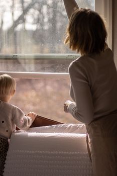 A serene moment of a mother and child looking out a bright window in a cozy room.
