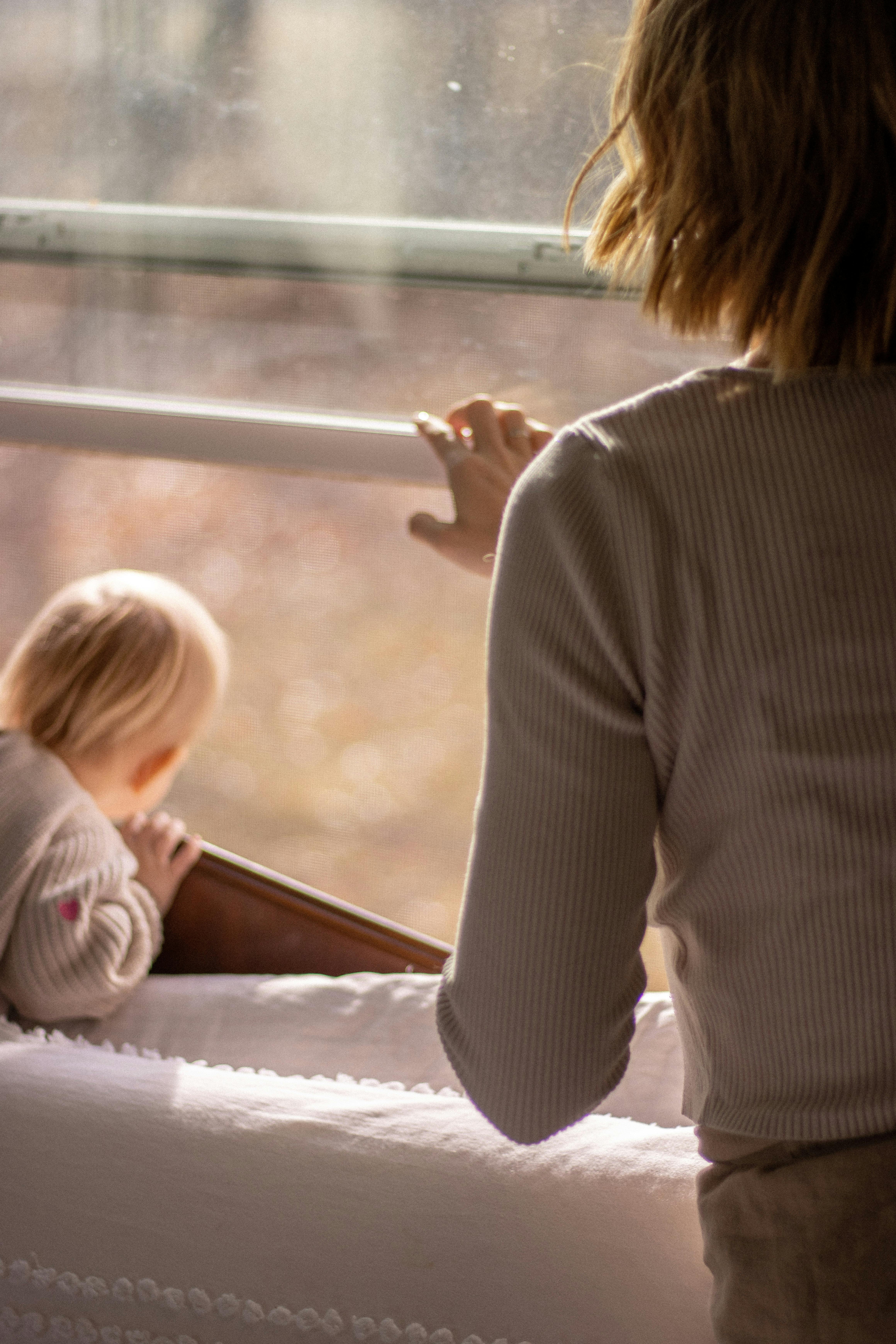 A serene moment of a mother and baby enjoying natural light by the window.