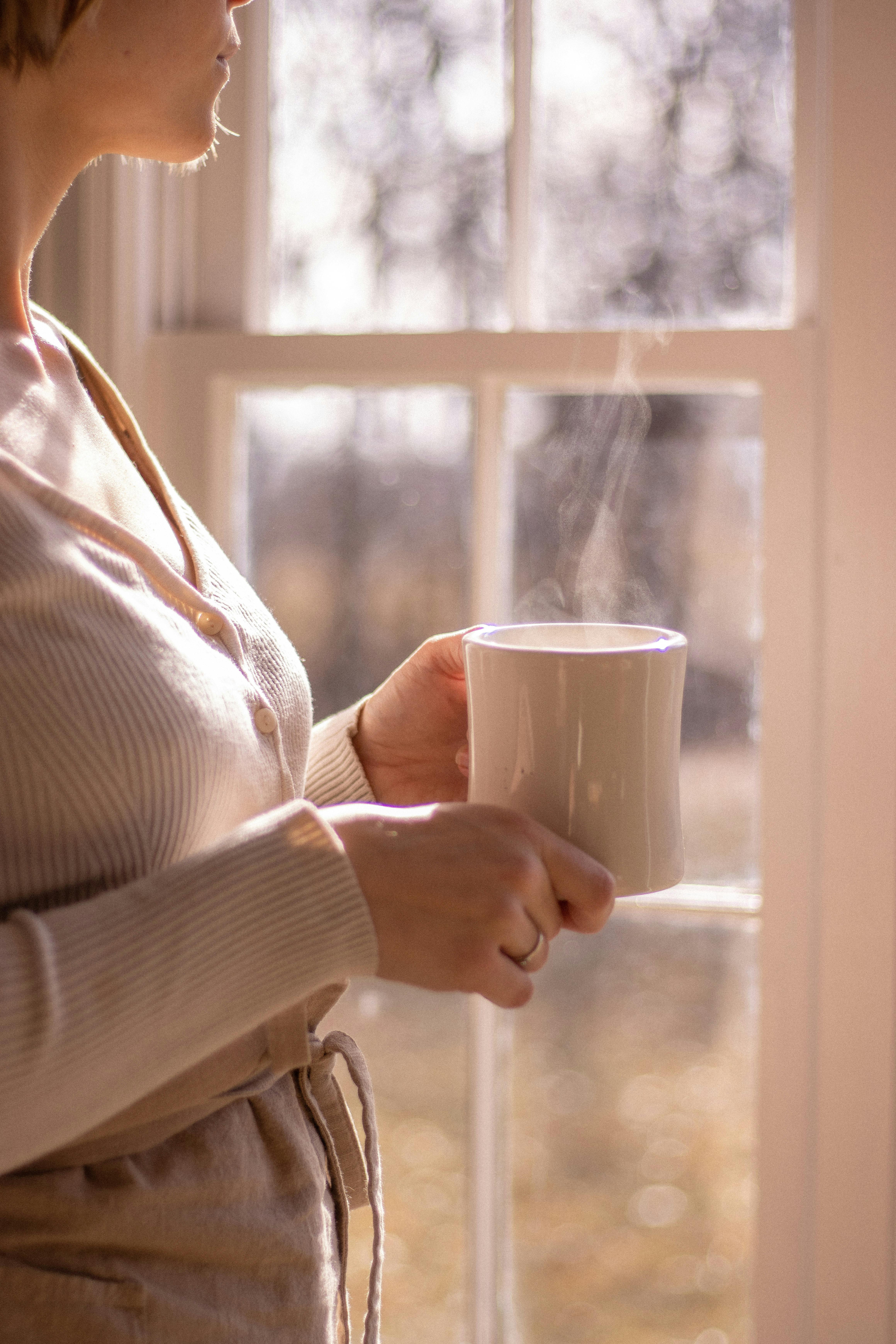 Hand holding coffee mug by bright window, soft morning light