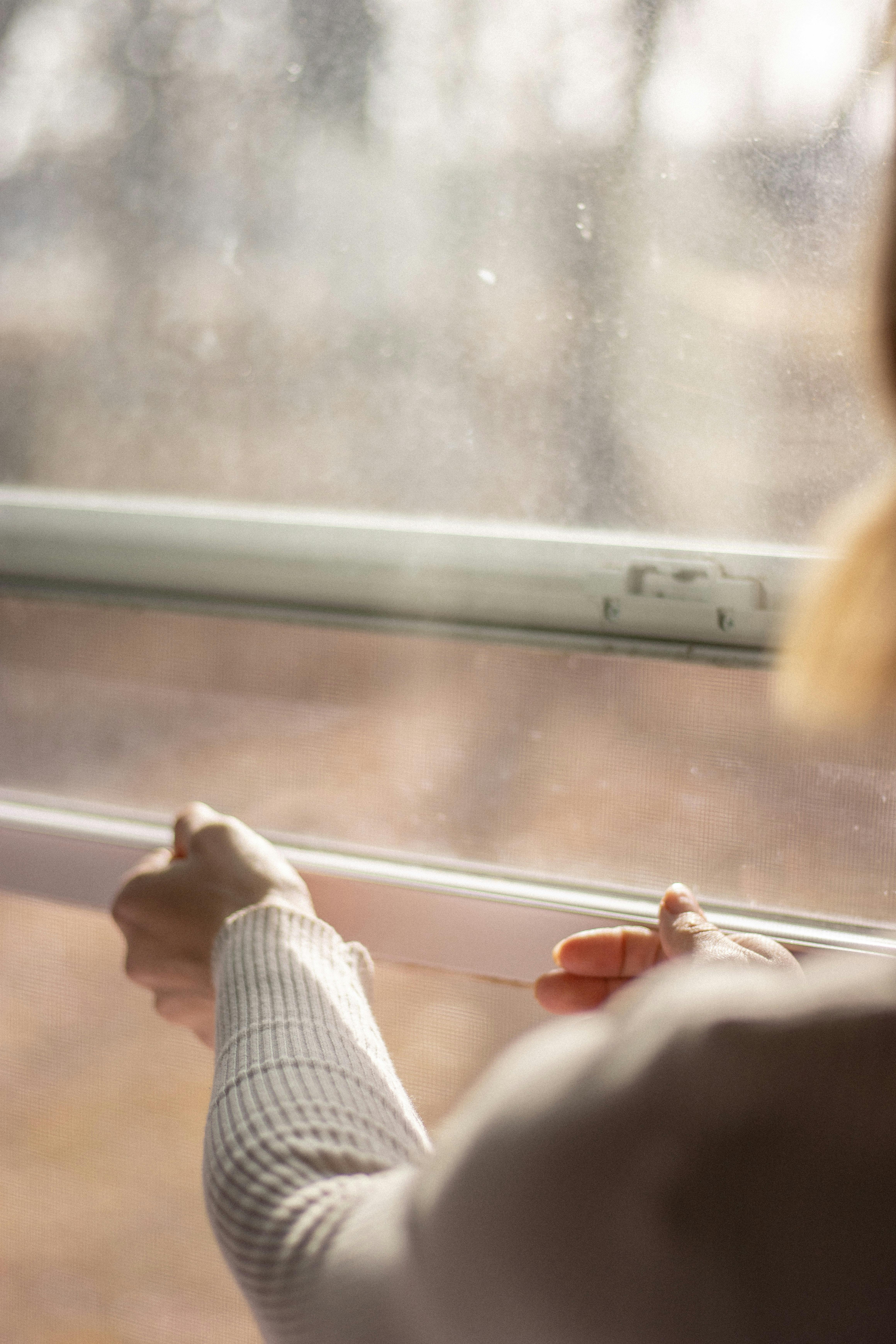 Elegant woman adjusting a modern window, showcasing natural light and minimalist design.