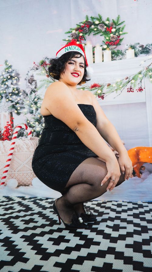 Free Woman in black dress with a Santa hat poses in festive Christmas setting. Stock Photo