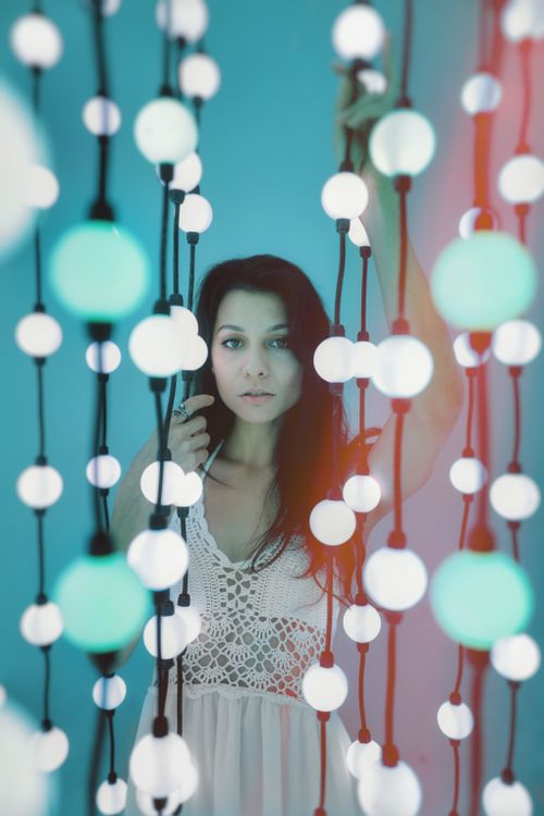 Free Artistic portrait of a woman surrounded by hanging spherical lights in a modern setting. Stock Photo