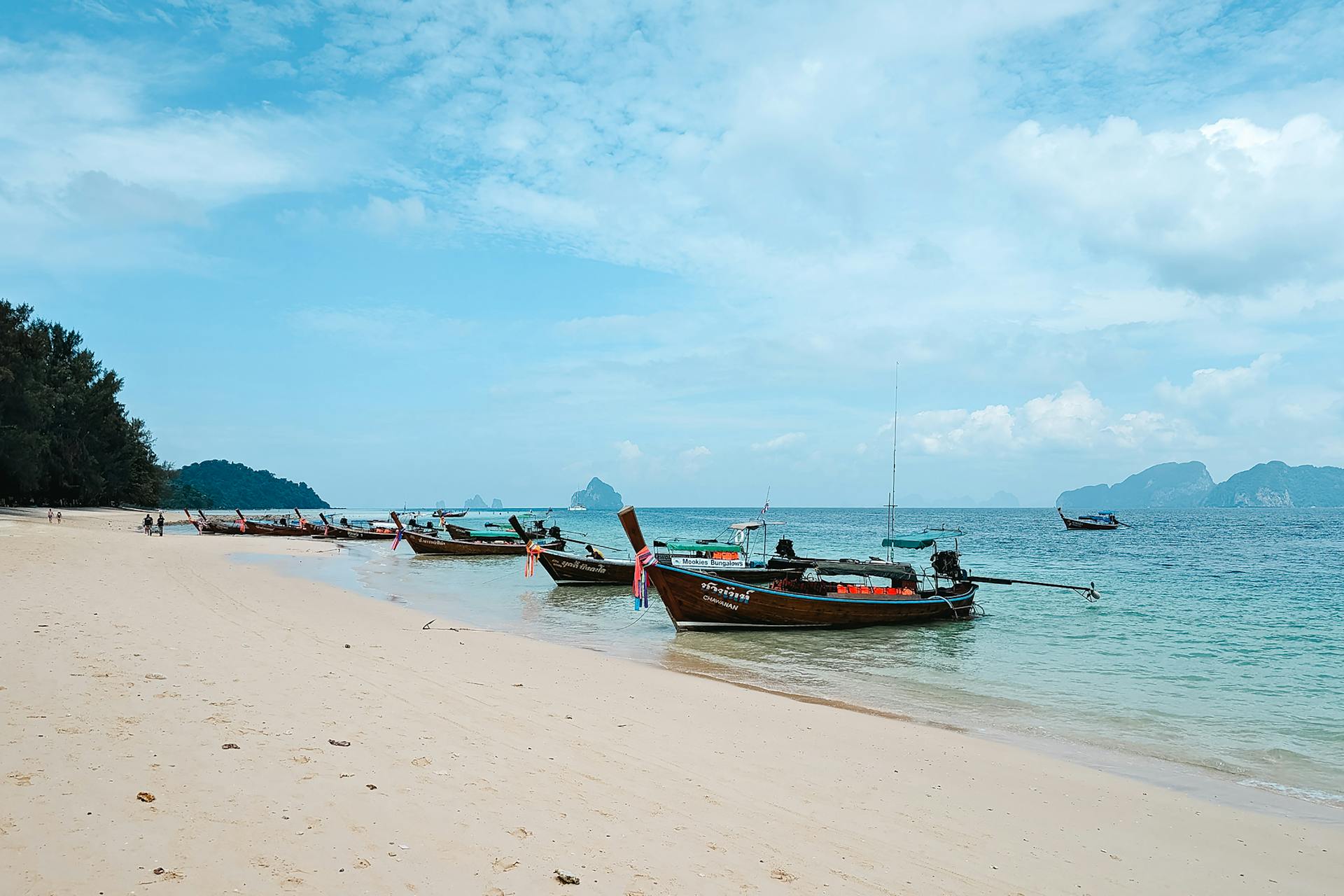 Serene Thai beach scene featuring longtail boats and tropical scenery under a blue sky.