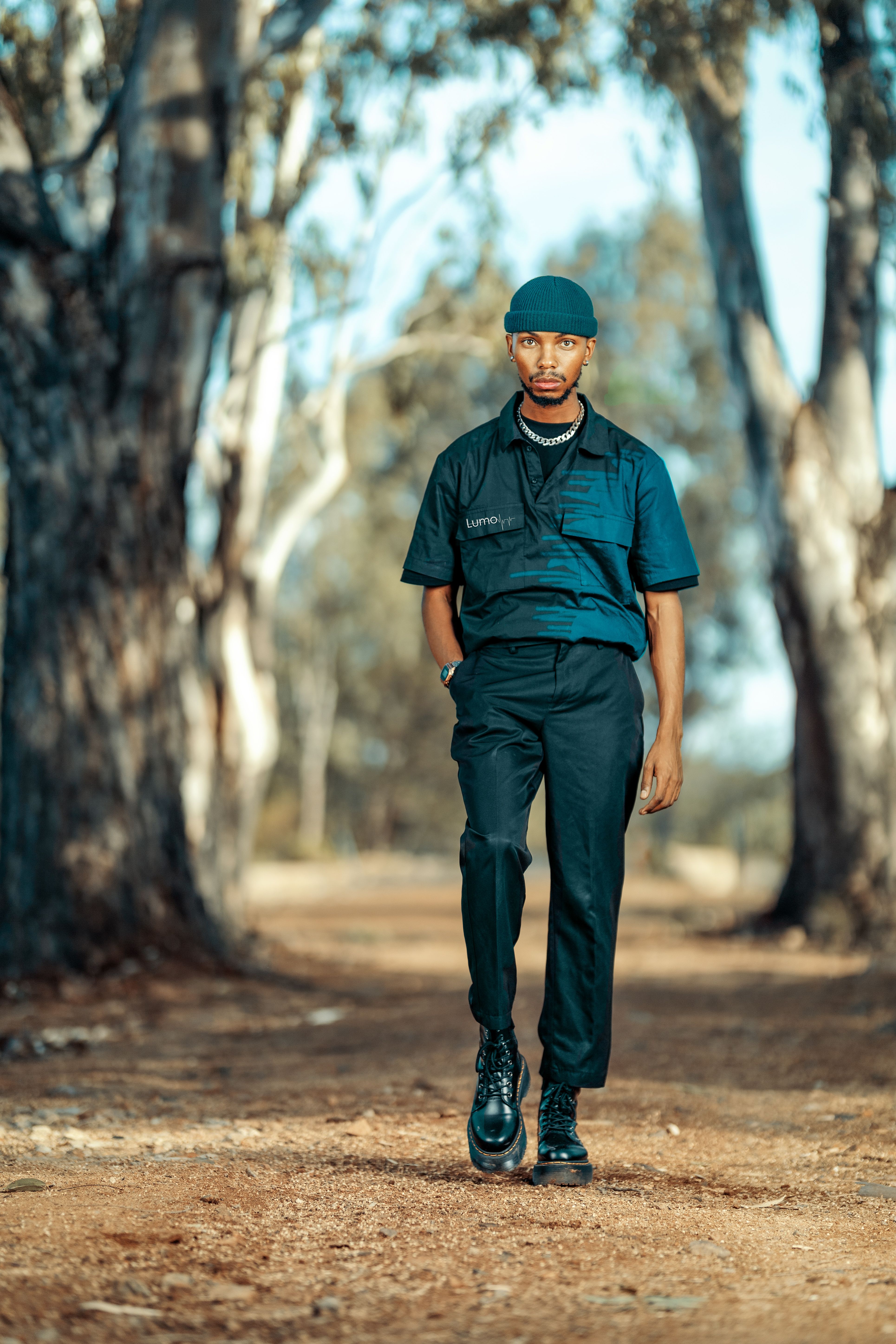 Young man in trendy attire strolling along a sunlit forest path, embodying confidence and style.