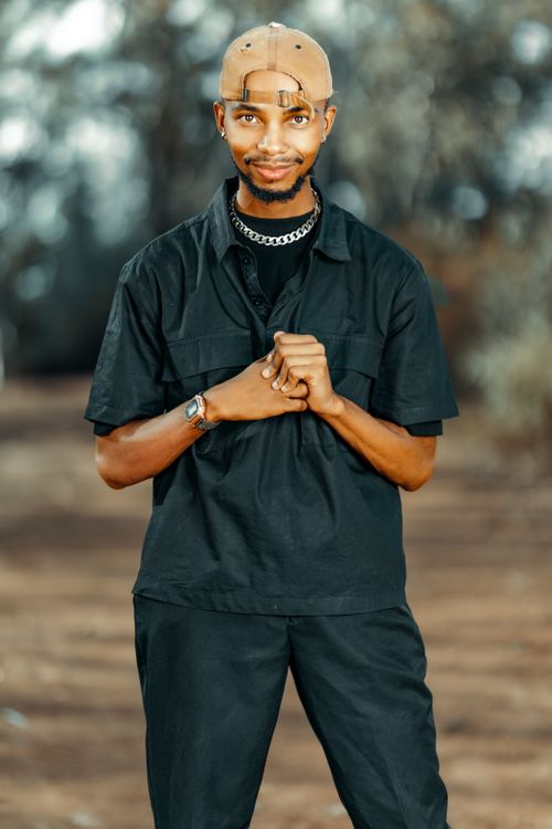 Free Man wearing a black outfit and cap standing outdoors, hands clasped. Stock Photo