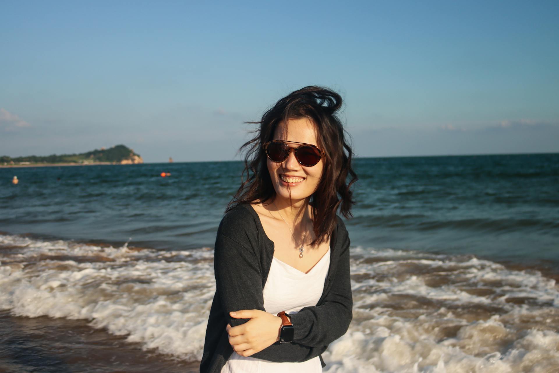 Happy woman in sunglasses enjoying the sunshine at a Qingdao beach with blue skies and ocean waves.