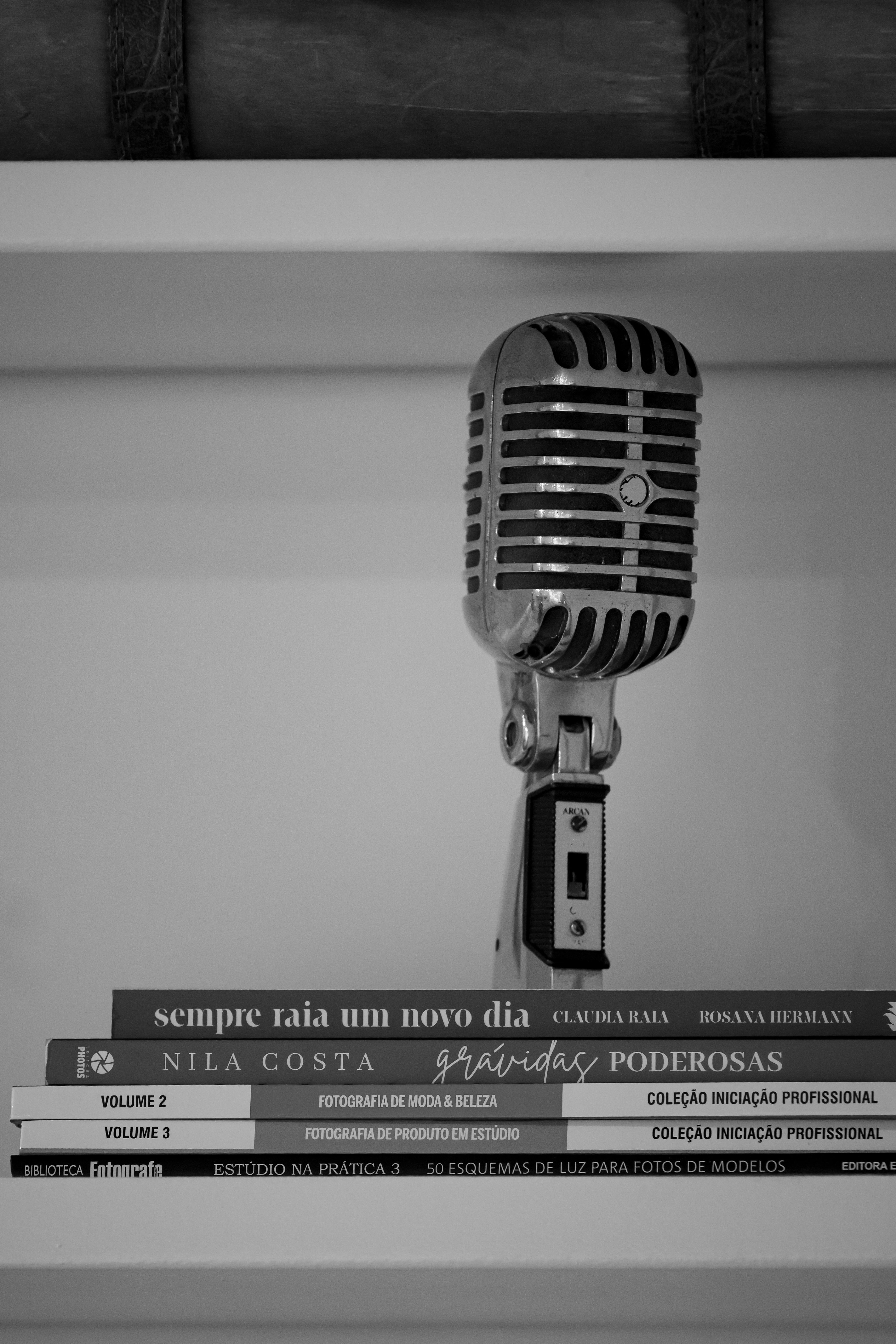 grátis Um microfone vintage clássico adorna uma pilha de livros, capturados em preto e branco. Foto profissional