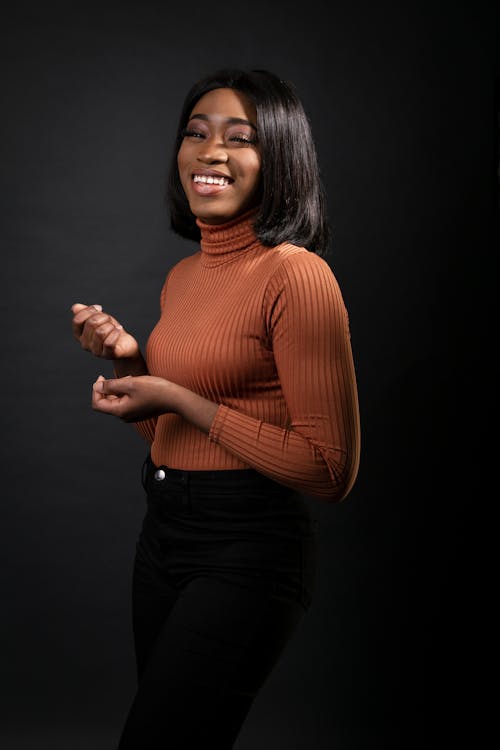 Free Photo of Laughing Woman in Brown Turtleneck Sweater and Black Pants Posing In Front of Black Background Stock Photo