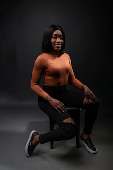 在深色背景的工作室里，时尚女性坐在椅子上摆姿势