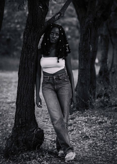 Black and white portrait of a woman leaning against a tree in a tranquil forest setting.