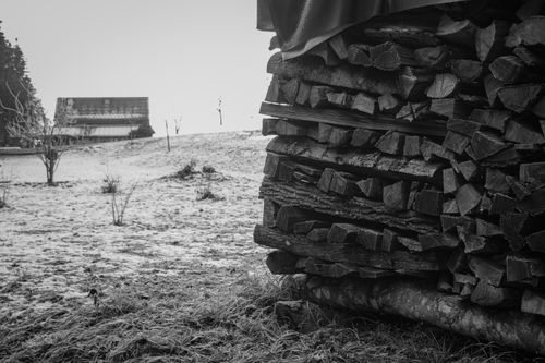 Free Black and white image of firewood stack and distant building in snowy landscape. Stock Photo