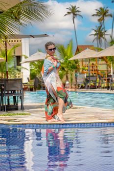 A fashionable woman in a summer dress enjoying a sunny day by a tropical pool.