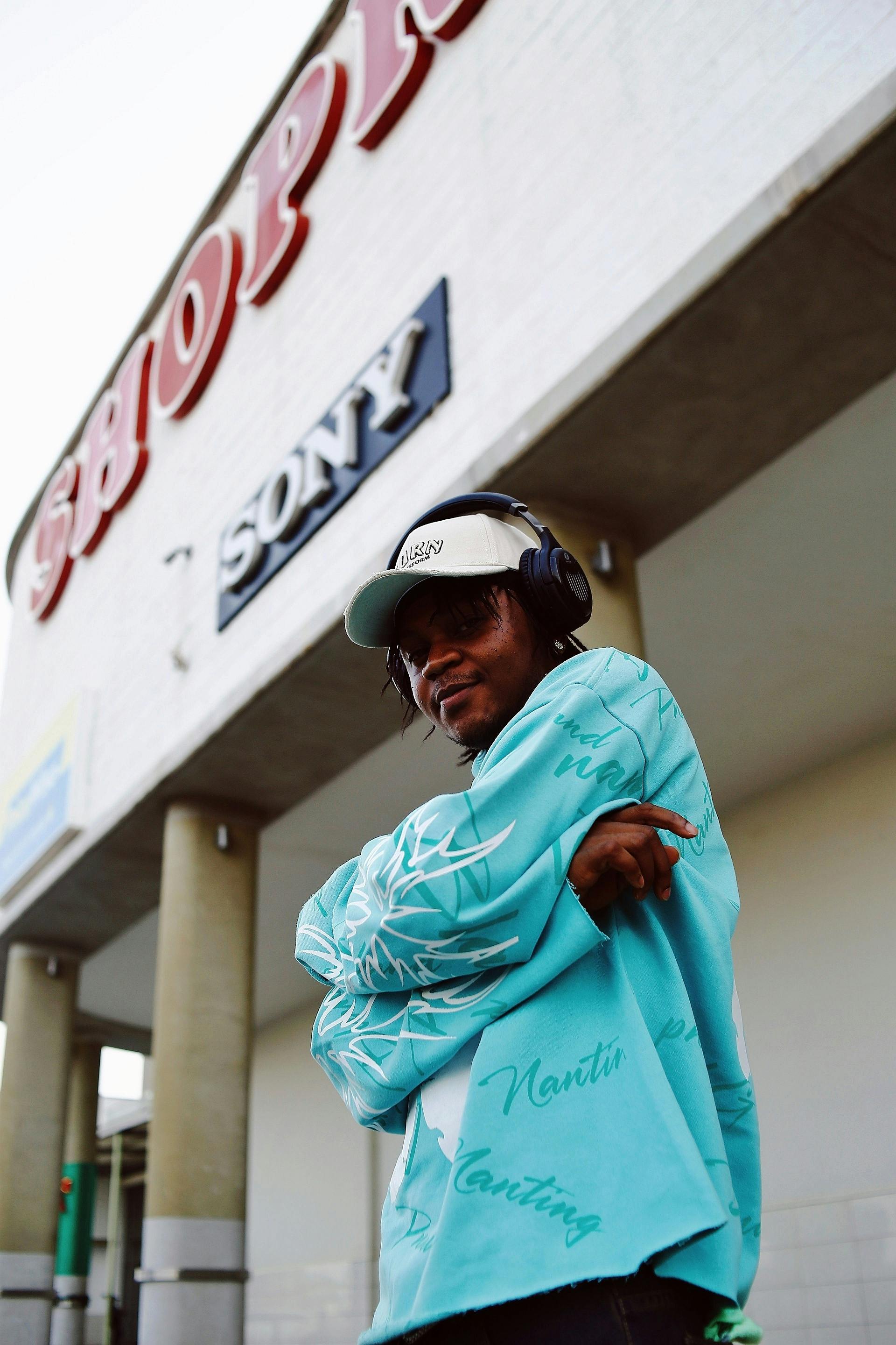 A fashionable young man wearing headphones poses in front of a shopping center in Abuja, Nigeria.