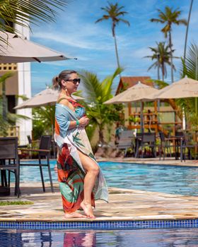 Stylish woman in colorful dress by a pool in a sunny tropical resort.