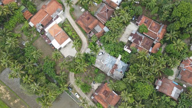 Aerial view of rural village with red roofs and lush green tropical vegetation.