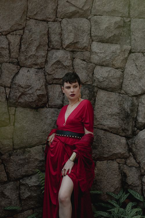 Free Fashionable woman in red dress poses against a rustic stone wall. Stock Photo