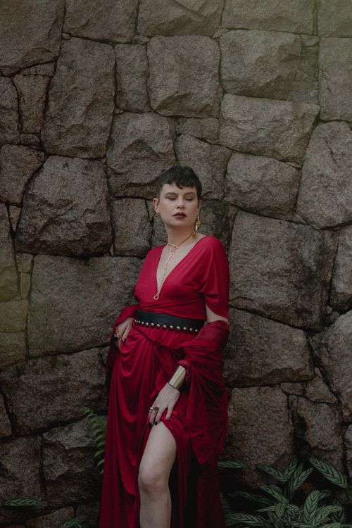 Free Stylish woman in red dress against a rustic stone wall in Curitiba, Brazil. Stock Photo