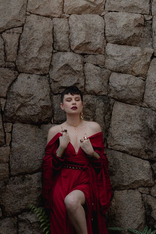 Free Stylish woman in a bold red dress posing against a rustic stone wall. Stock Photo