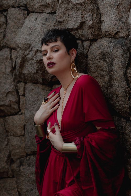 Free Stylish woman in a red dress posing against a stone wall, exuding modern elegance. Stock Photo