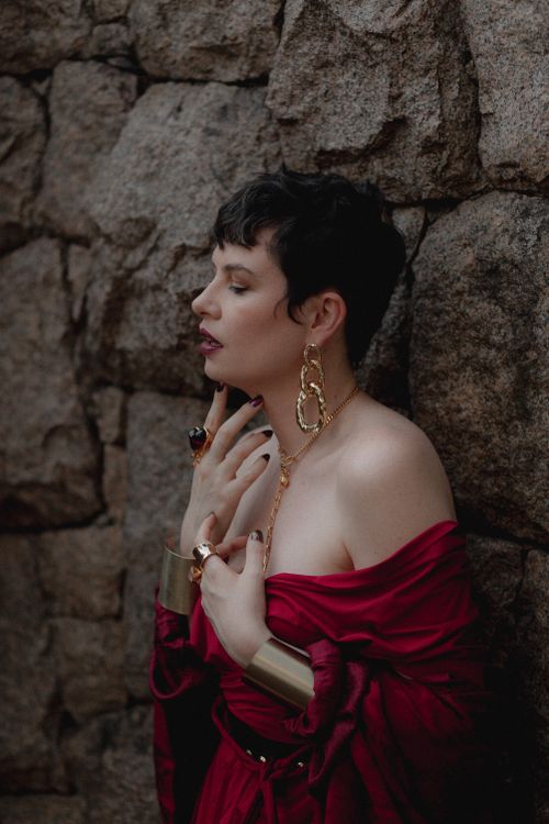 Free Portrait of a woman in a red dress against a textured stone wall, exuding elegance. Stock Photo